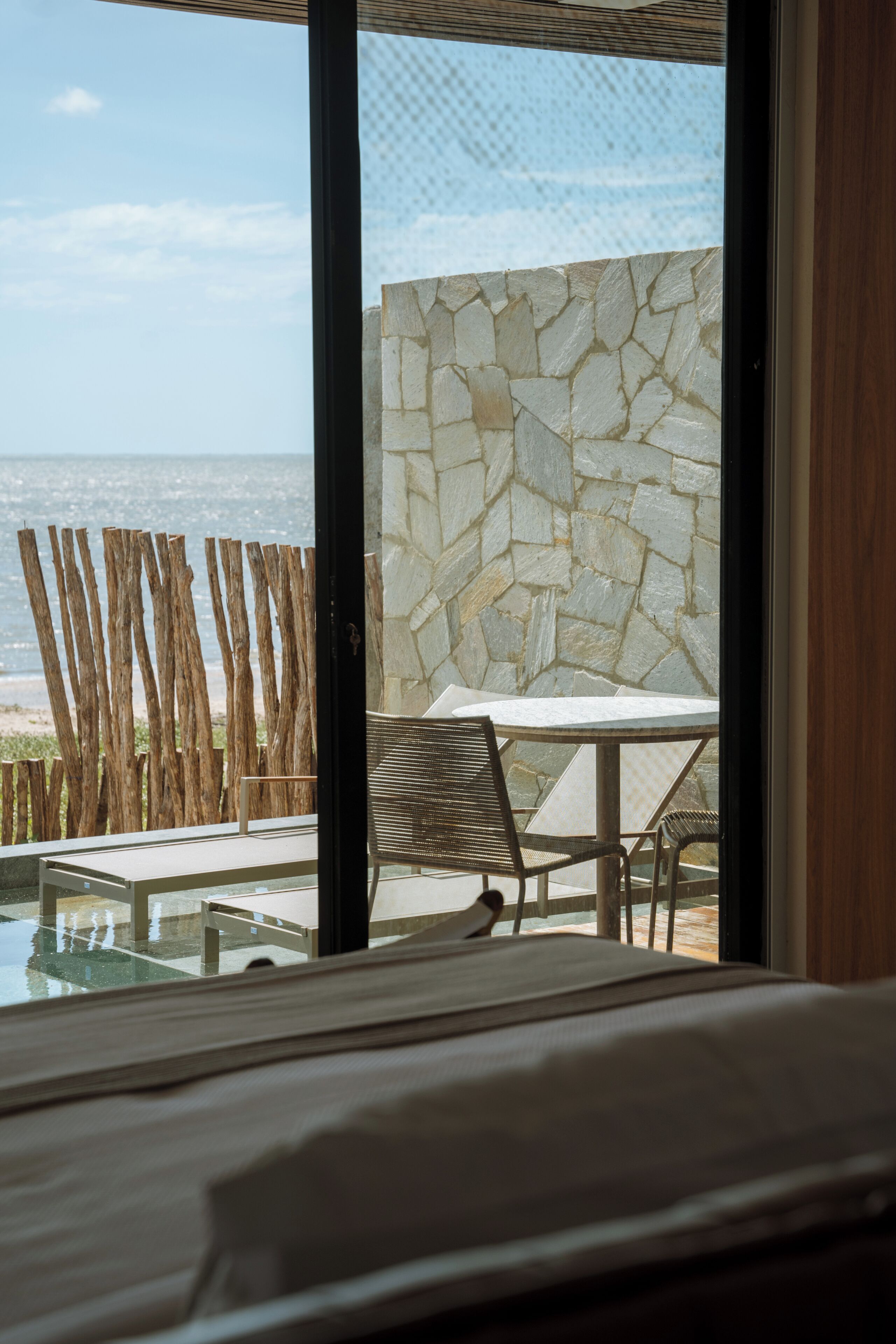 Quarto com vista para o oceano, parede de pedra e uma mesa com cadeiras.