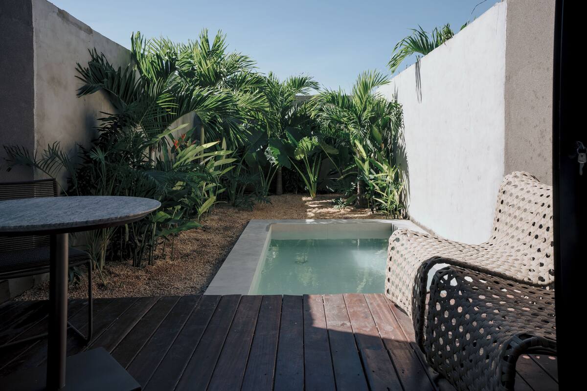 A pool area with a wooden deck, a round table, and a wicker chair.