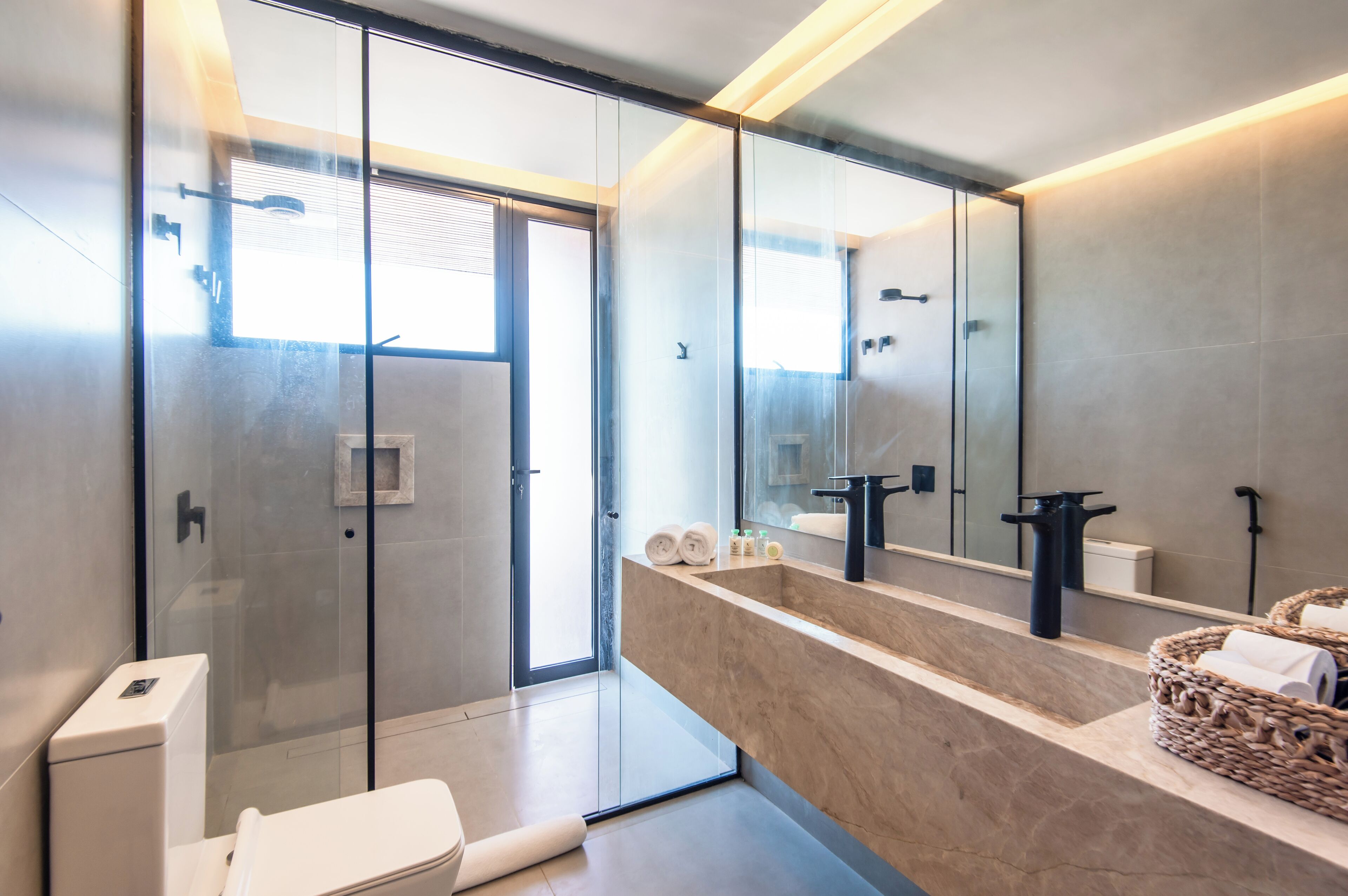 A modern bathroom with a glass-enclosed shower, a large mirror, and a marble countertop.