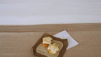 A neatly made bed with a brown bedspread and two pillows, a tray with two pastries, and a note on the bed.