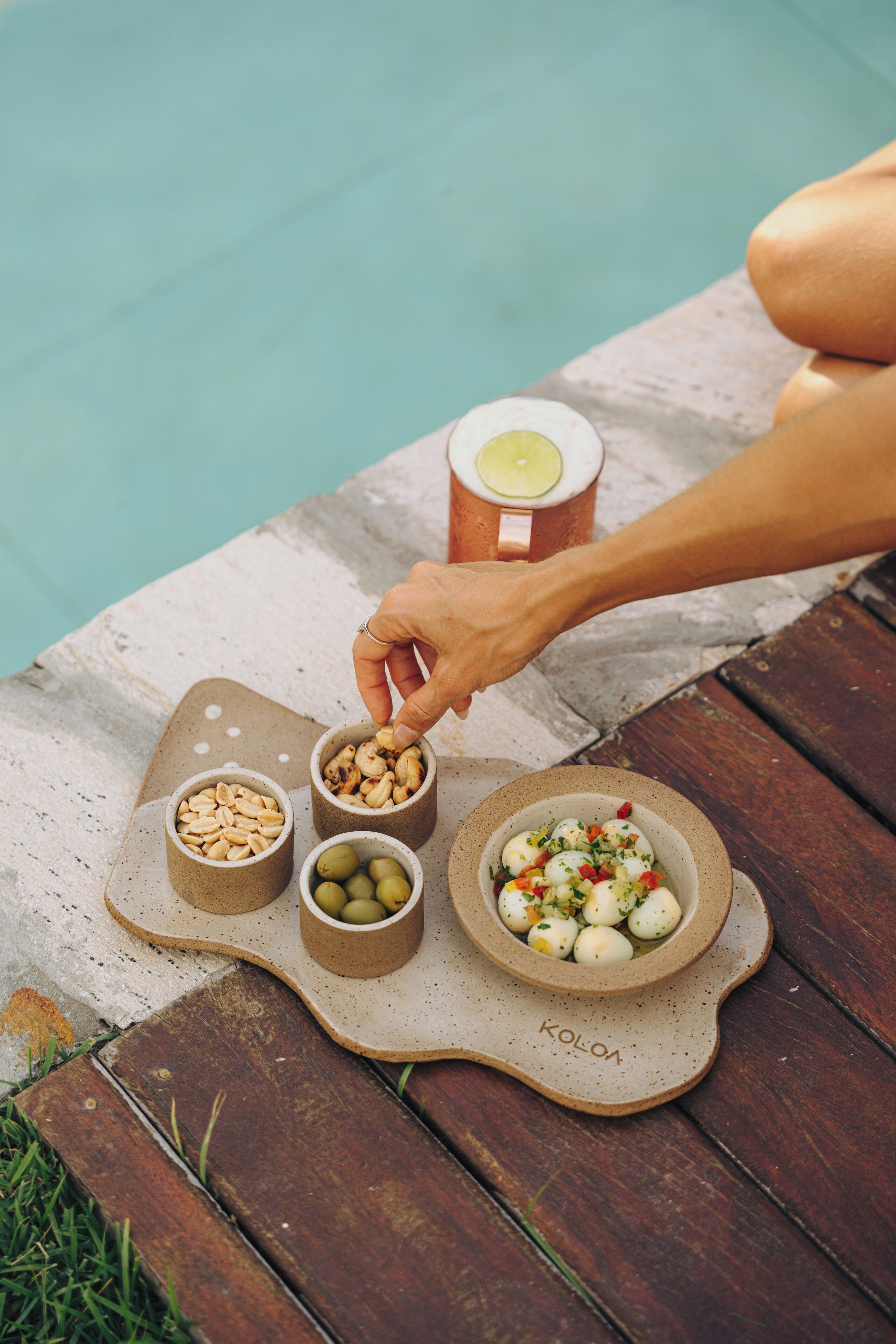 A wooden table with a snack tray containing nuts, olives, and a bowl of mixed vegetables.