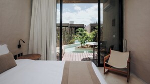 Quarto com cama, uma cadeira de madeira, uma mesinha e vista para a área da piscina.