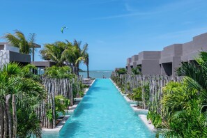 A clear blue pool with a straight path leading to the sea, surrounded by palm trees and modern buildings. - Koloa Concept Hotel (Cajueiro da Praia)