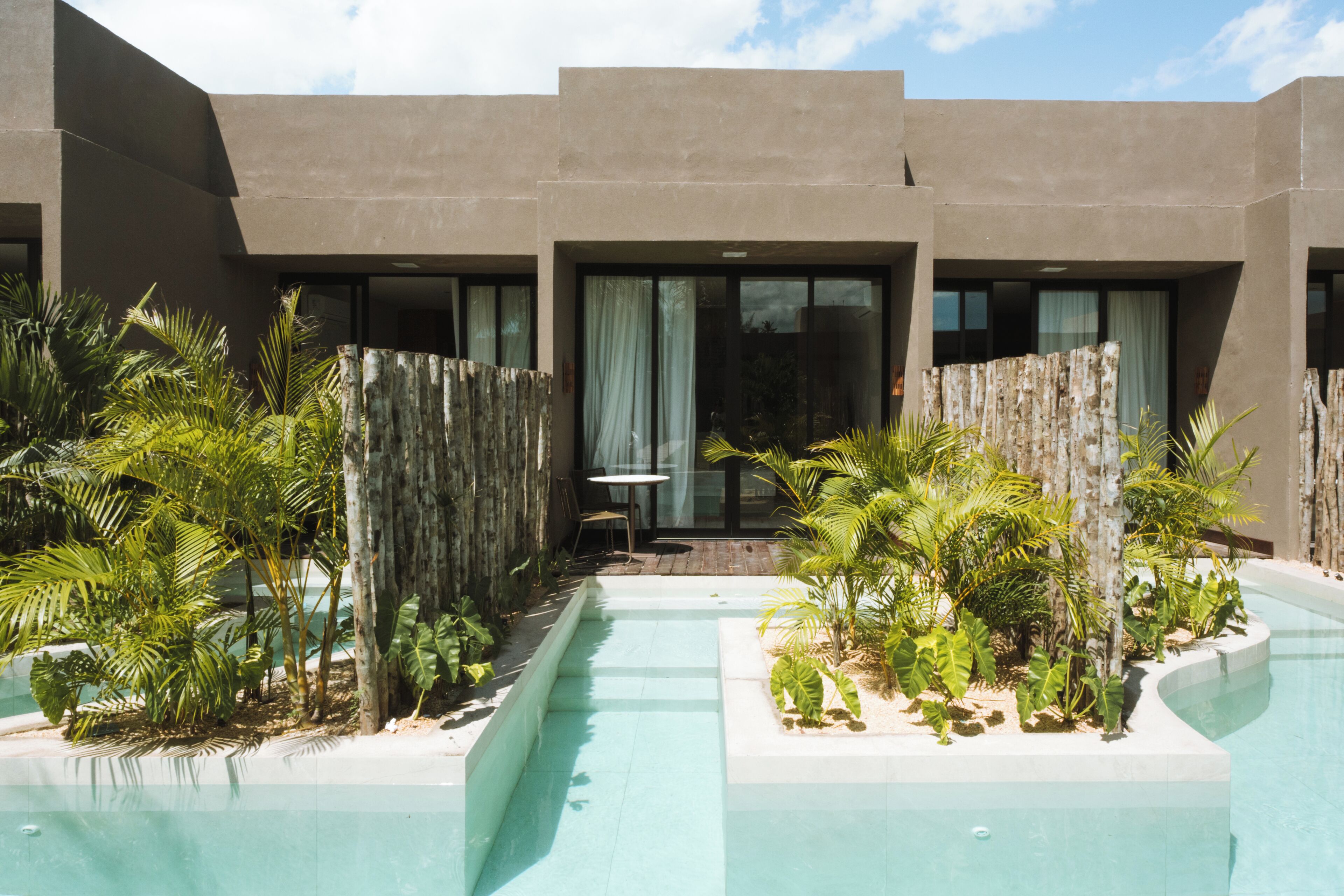 Un bâtiment moderne doté d’une piscine, entouré de plantes tropicales et d’une clôture en bois.