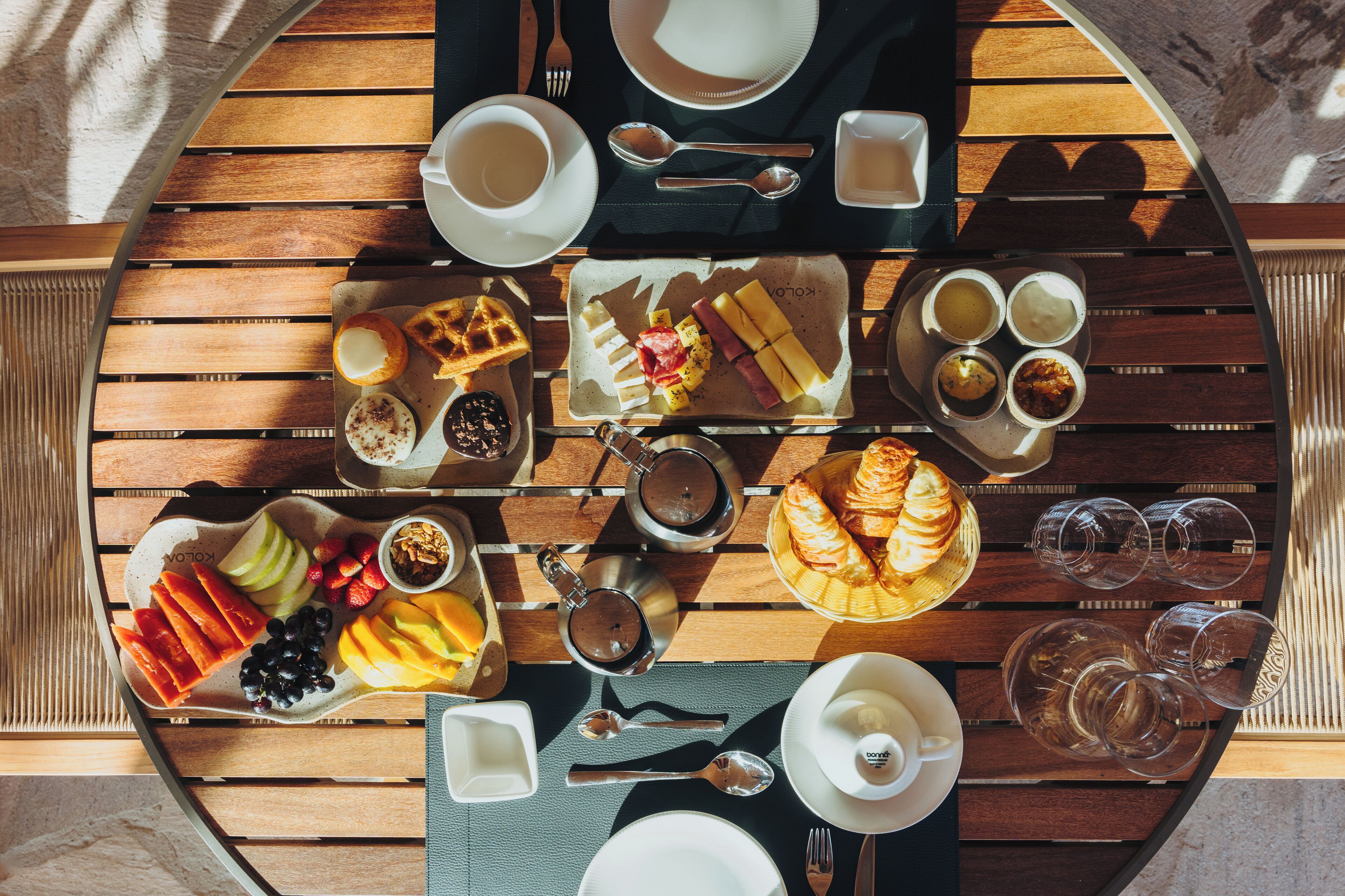 A breakfast setting with a variety of food items, cups, and cutlery on a wooden table.