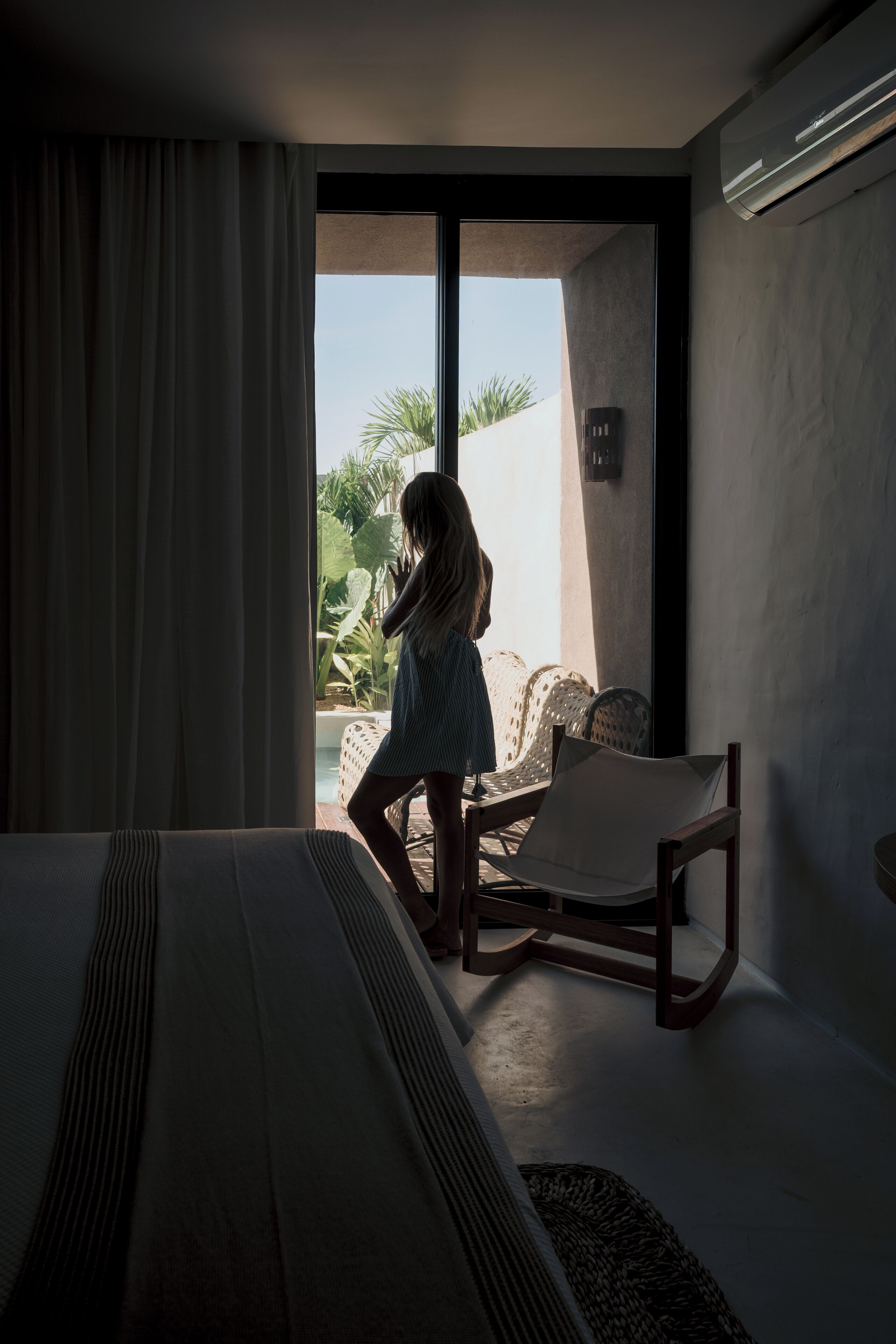 A hotel room with a bed, a chair, and a view of the outdoors.