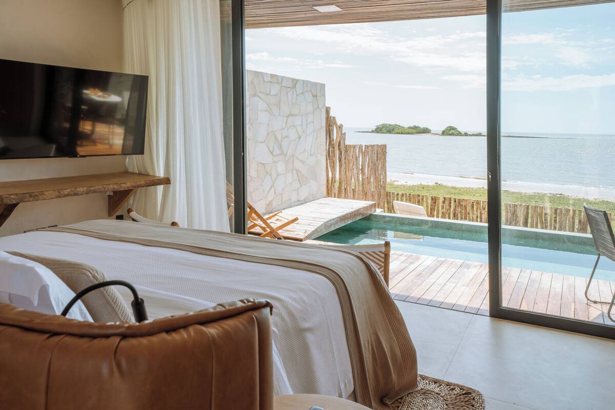 A bedroom with a large window overlooking a pool and beach.