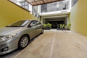 A car parked in a covered parking area with a building entrance labeled 'AVALON' in the background. - Reddoorz Plus @ Pasar Baru (Jakarta)