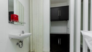 A bathroom with a white sink, a mirror, a red toiletry bag, a black cabinet, and a shower curtain. - Reddoorz Plus @ Pasar Baru (Jakarta)
