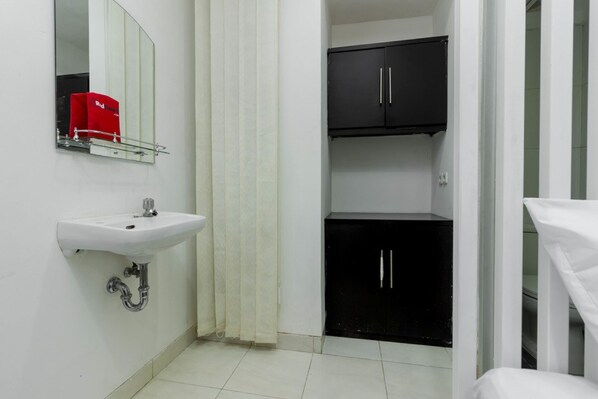 A bathroom with a white sink, a mirror, a red toiletry bag, a black cabinet, and a shower curtain. - Reddoorz Plus @ Pasar Baru (Jakarta)
