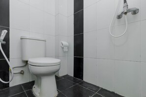 A bathroom with a toilet, a hand shower, and a toilet paper holder. - Reddoorz Plus @ Pasar Baru (Jakarta)