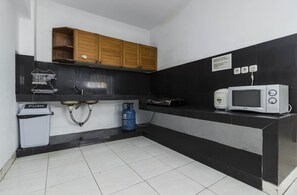 A compact kitchen with black and white tiles, wooden cabinets, a gas stove, a microwave, and a push-button trash bin. - Reddoorz Plus @ Pasar Baru (Jakarta)