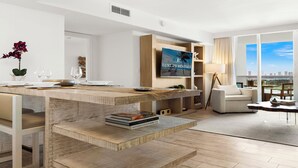 A modern living room with a wooden coffee table, a flat-screen TV, a sofa, and a view of the city.