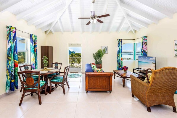 A spacious living area with a dining set, a television, and a view of the beach. - Chalk Sound | Lagoon Views | Walk to Sapodilla Bay (Providenciales)