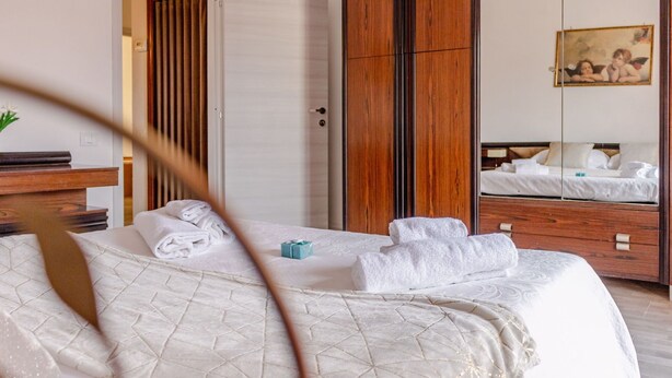 A hotel room with a bed, a wooden wardrobe, a mirror, and a painting on the wall. - Italian Experience- Maison Loreto (Loreto)