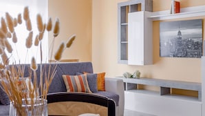 A modern living room with a grey sofa, colorful cushions, a vase with dried plants, a white console table, and a cityscape painting on the wall. - Italian Experience- Maison Loreto (Loreto)