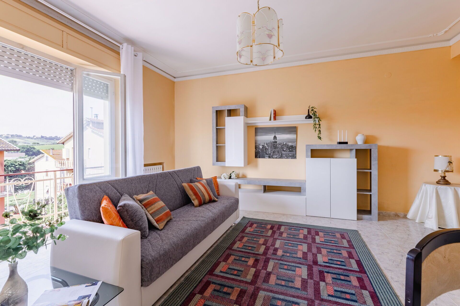 A living room with a grey sofa, patterned rug, and a cityscape painting on the wall.