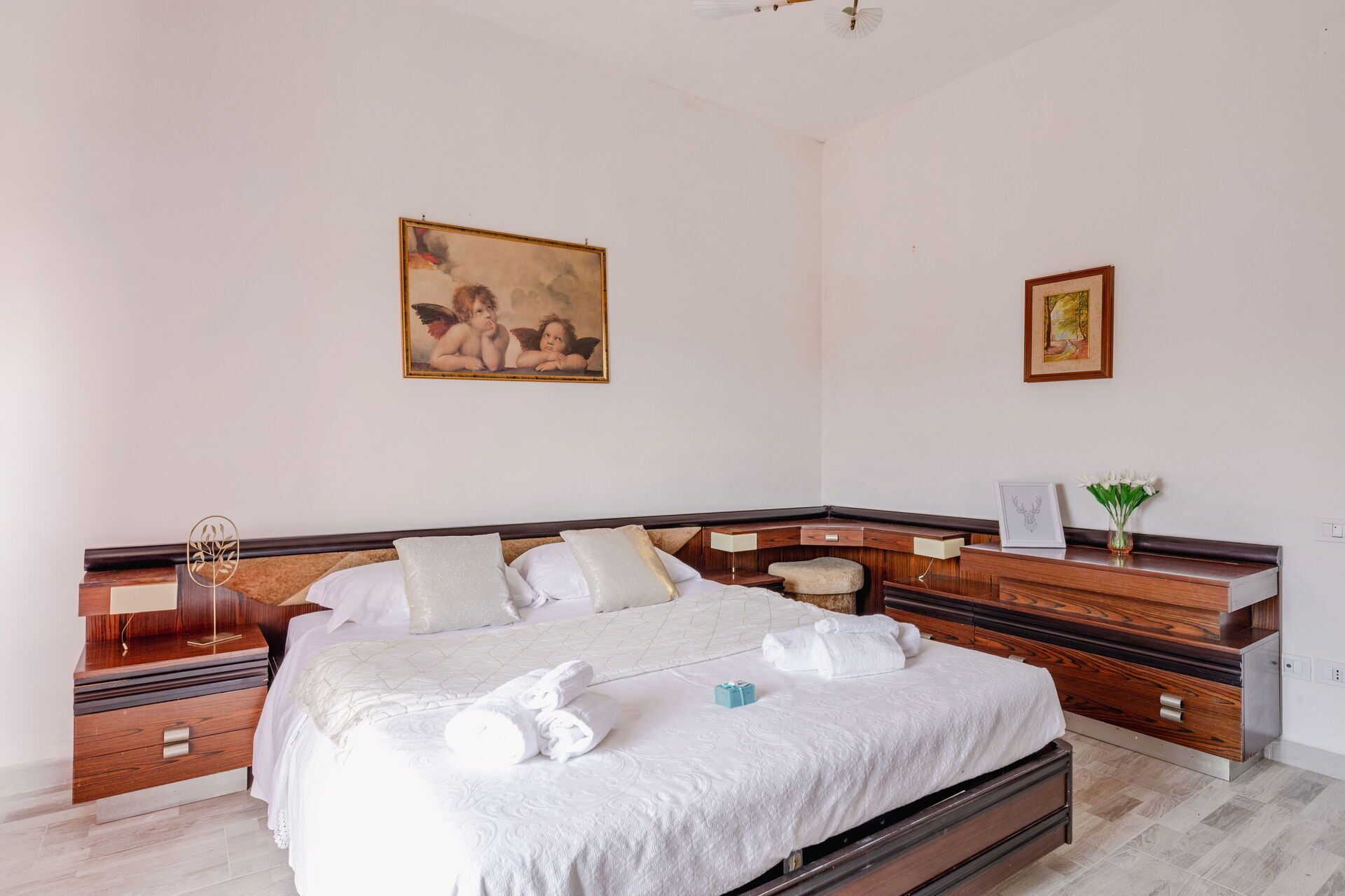 Un dormitorio ordenado con una cama, mesitas de noche y obras de arte en las paredes.