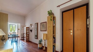 A spacious room with hardwood flooring, a wooden bookshelf, a dining area with chairs, and a large wooden door.