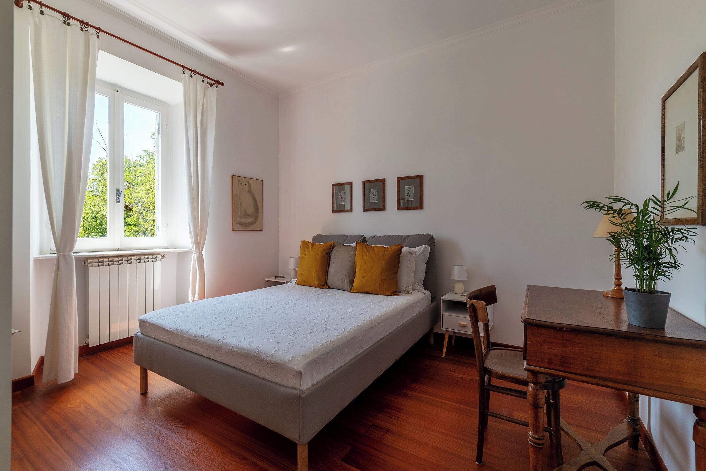 A bedroom with a bed, a nightstand, a chair, a desk, and a potted plant.