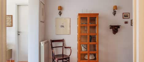 A room with a wooden chair, a cabinet with glass doors, and wall-mounted lamps.