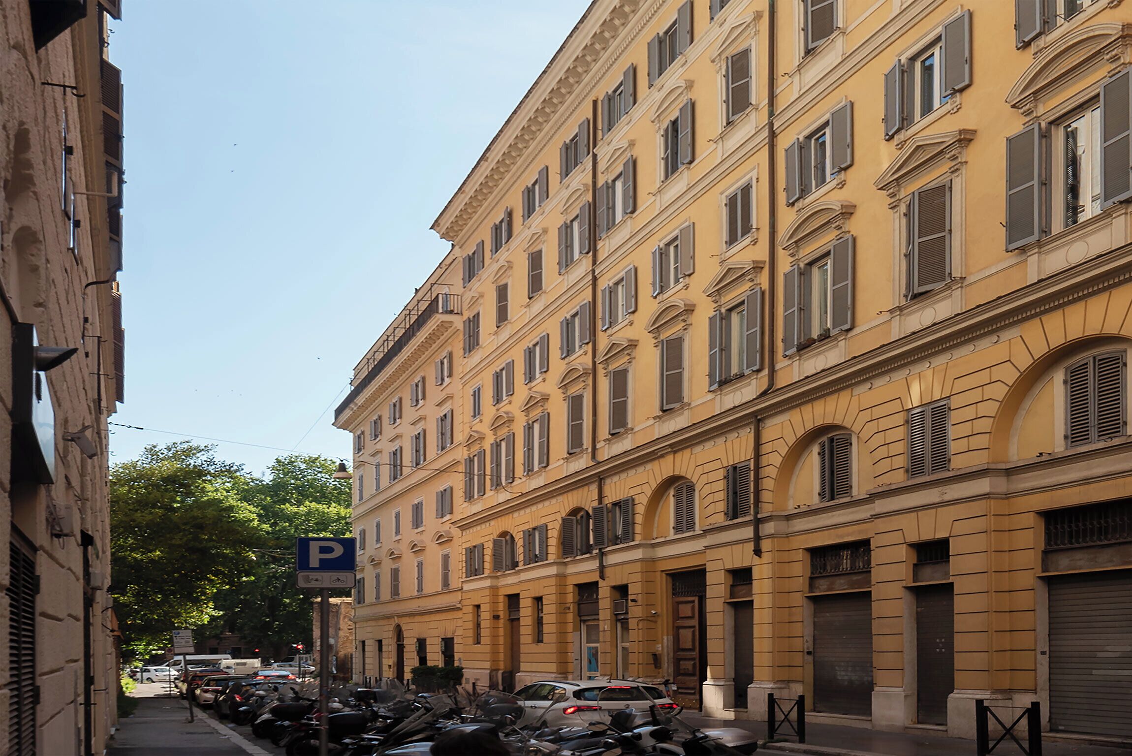 Eine schmale Straße, gesäumt von parkenden Autos und einer Reihe gelber Gebäude mit zahlreichen Fenstern und Fensterläden.