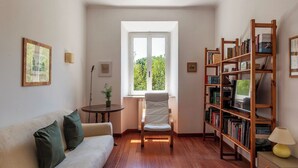 A cozy living room with a sofa, a chair, a bookshelf, and a window with a view of greenery.