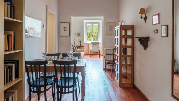 A dining area with a wooden table and chairs, a bookshelf, and a view of a living room through an open door.