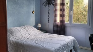 Un dormitorio con cama, mesita de noche, lámpara, ventana con cortinas y un adorno en la pared.