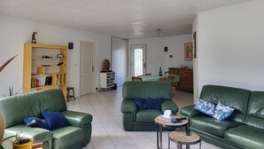 Una sala de estar con sofás de cuero verde, una estantería de madera y un comedor con mesa y sillas.