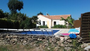 Un muro de piedra, una piscina y una casa con techo de tejas.