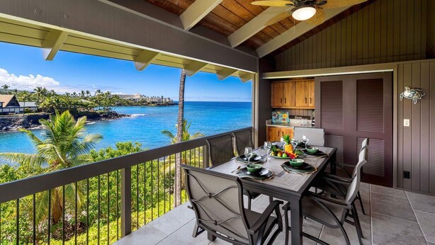 Un balcone con tavolo apparecchiato per mangiare, vista sulla costa, soffitto in legno e ventola a soffitto.