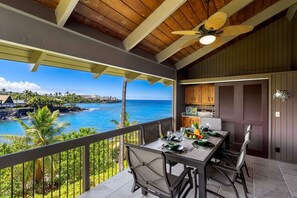 Un balcon avec une table dressée pour le dîner, offrant une vue sur la côte, doté d’un plafond en bois et d’un ventilateur de plafond.