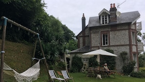 A stone house with a garden, a hammock, striped lounge chairs, and a table with an umbrella.