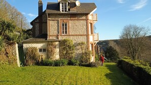 A large, two-story stone house with a well-maintained lawn and a small garden area.