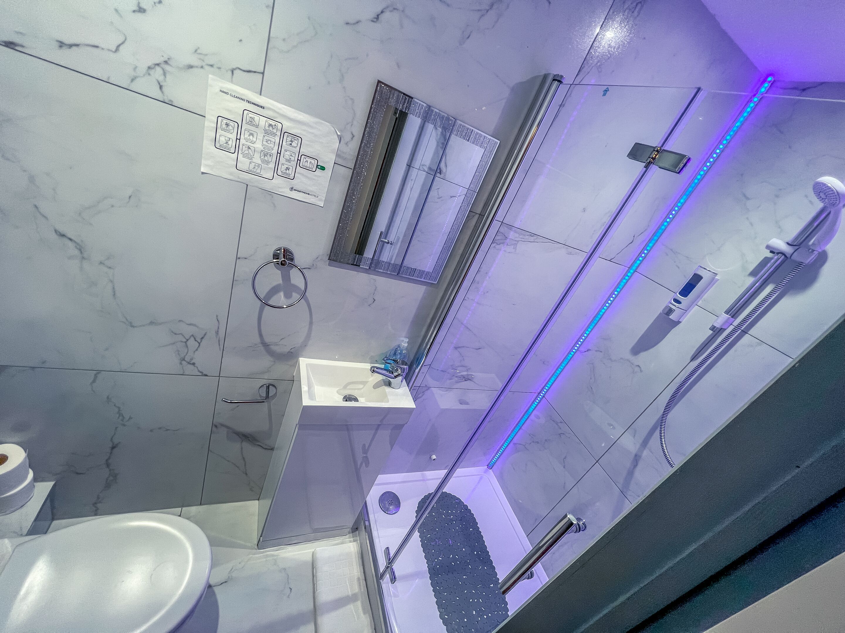 A bathroom with a marble floor, a sink, a toilet, and a shower area with blue LED lights.