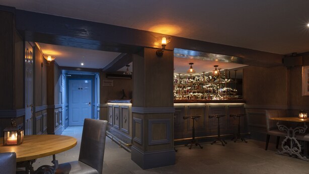 Una zona de bar con mostrador de madera, taburetes y una estantería con una amplia selección de licores.