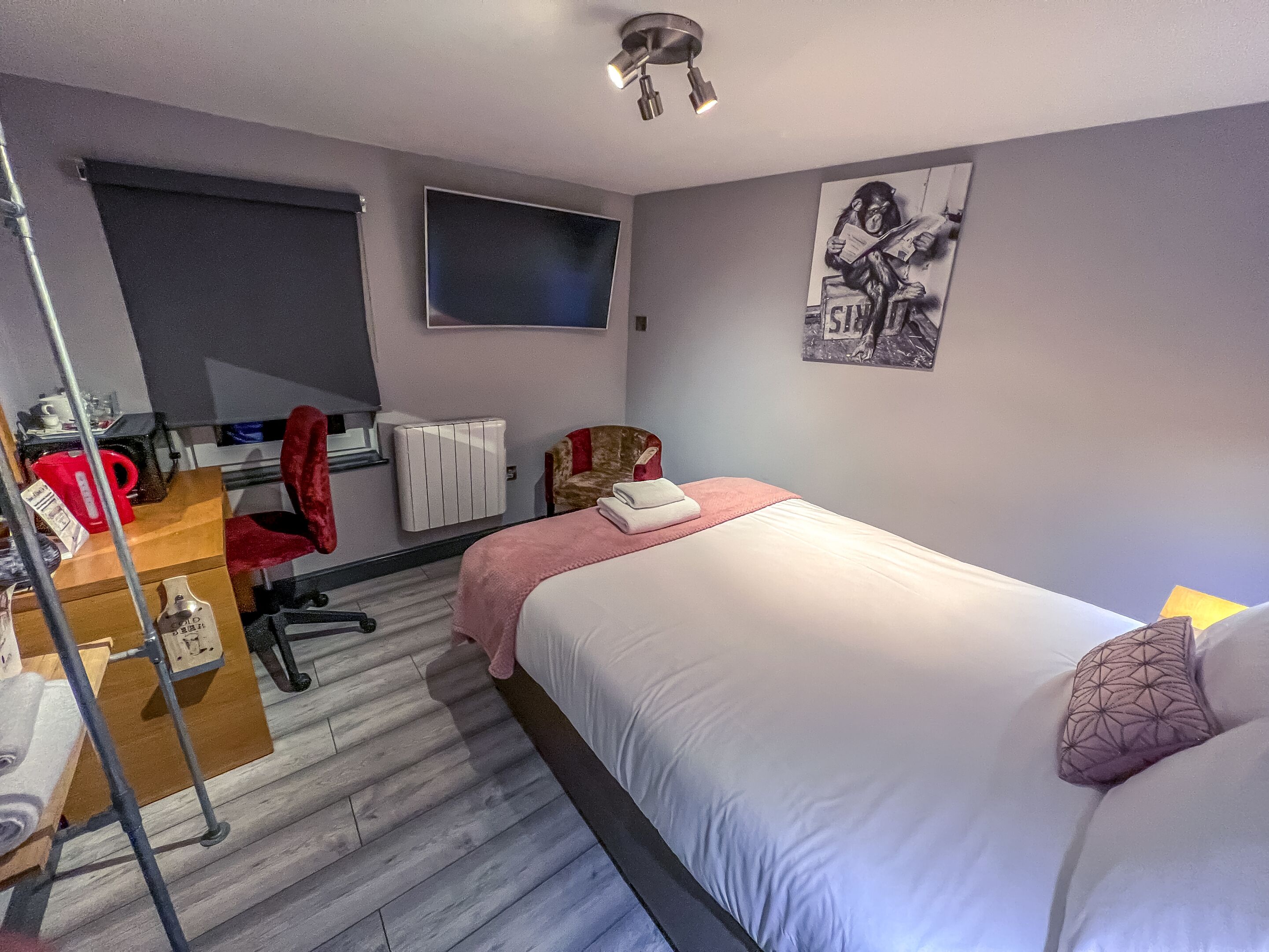 A hotel room with a bed, a desk, a chair, a radiator, and a television on the wall.