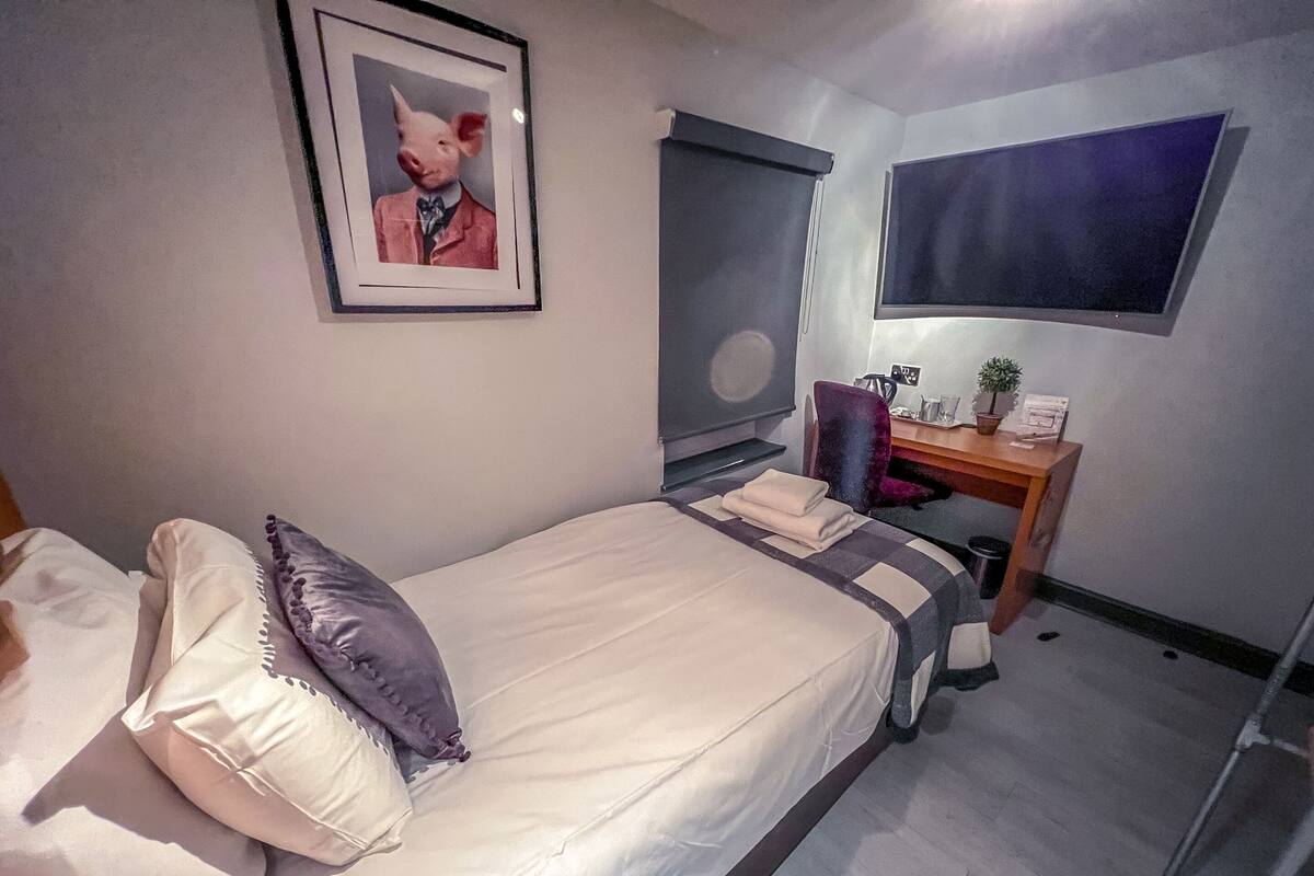 A bedroom with a bed, a desk, a chair, a window, and a framed picture on the wall.