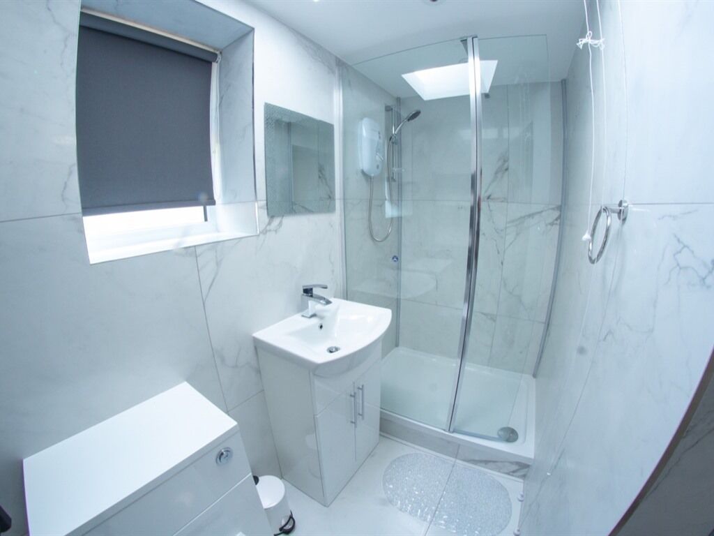 Un baño moderno con cabina de ducha de vidrio, un lavamanos blanco y suelo de baldosas de mármol.