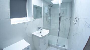 A modern bathroom with a glass shower enclosure, a white sink, and a marble-tiled floor.
