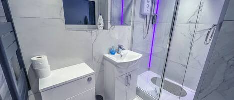 Un baño moderno con ducha de vidrio, lavamanos blanco y retrete.