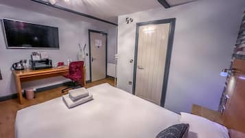 Quarto de hotel com cama, escrivaninha, computador, cadeira, televisão e porta.