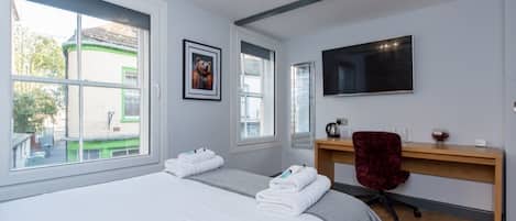 A hotel room with two beds, a desk, a chair, a TV, and large windows.
