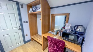 Habitación de hotel compacta con escritorio de madera, sillón cómodo, microondas, estante con artículos de aseo y espejo.