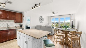 A modern kitchen with white cabinets, a granite countertop, and a dining area with a round table and wooden chairs. - Lakefront resort condo w/ pools & daily tickets (Panama City Beach)