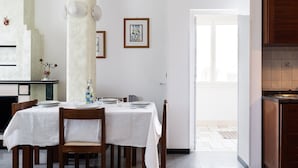 Een eethoek met een tafel gedekt voor vier personen, een kroonluchter en ingekaderde kunstwerken aan de muur.
