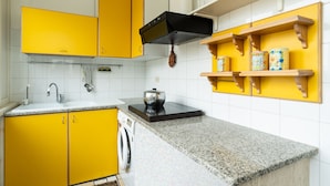 Een keuken met gele kastjes, een zwarte afzuigkap, een granieten aanrechtblad en houten planken met decoratieve spullen.