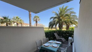 An outdoor patio with a table set for two, surrounded by chairs, and palm trees in the background. - Studio in Saint-Cyprien – Beach access, pool, terrace (Saint-Cyprien)