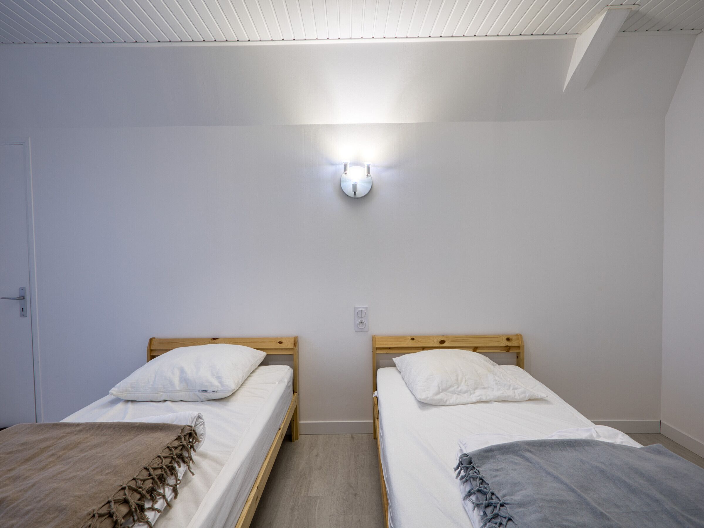 A room with two single beds, a light fixture on the wall, and a door on the left.